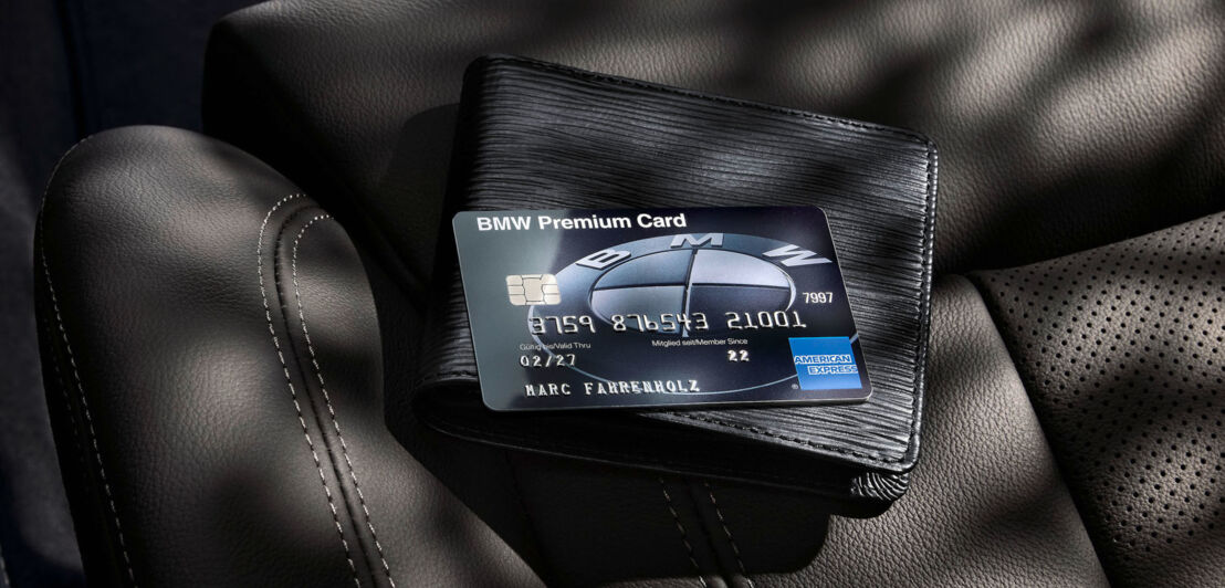 Eine schwarze BMW Premium Card von American Express legt auf einem schwarzen Portemonnaie auf einem Autositz aus schwarzem Leder.