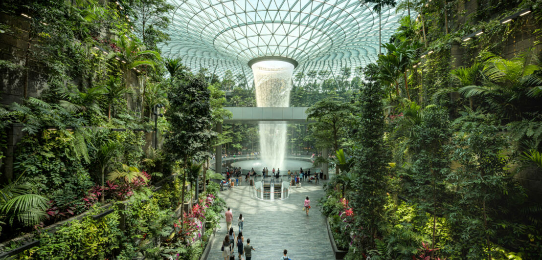 Personen an einem Wasserfall in einem vertikalen Garten in einem Flughafenterminal.