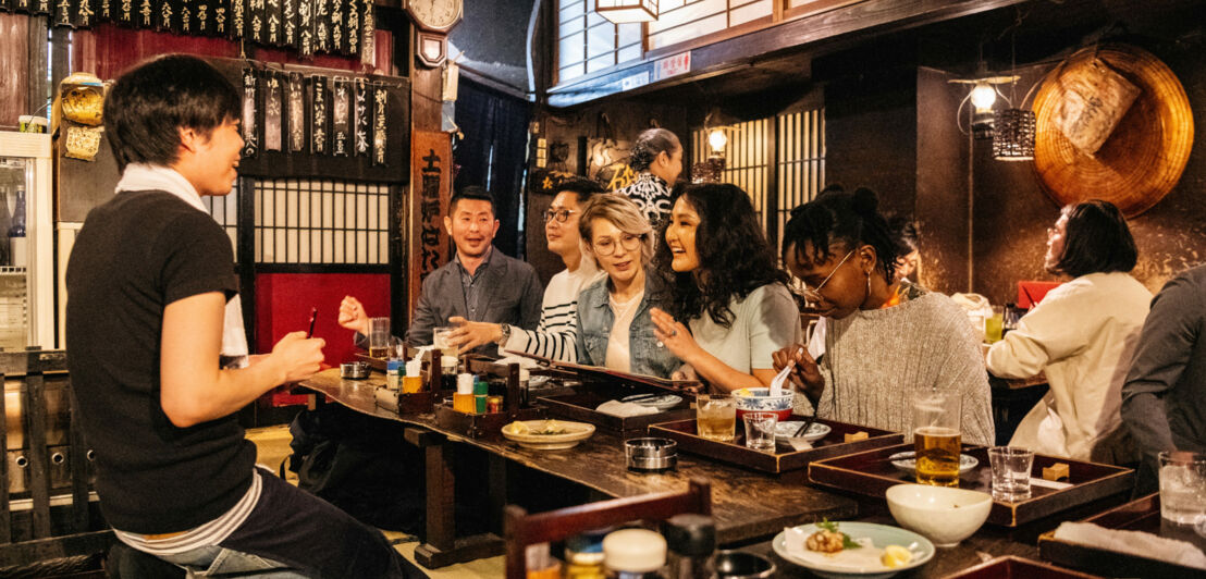 Mehrere Personen sitzen an einem Tresen in einem japanischen Restaurant.