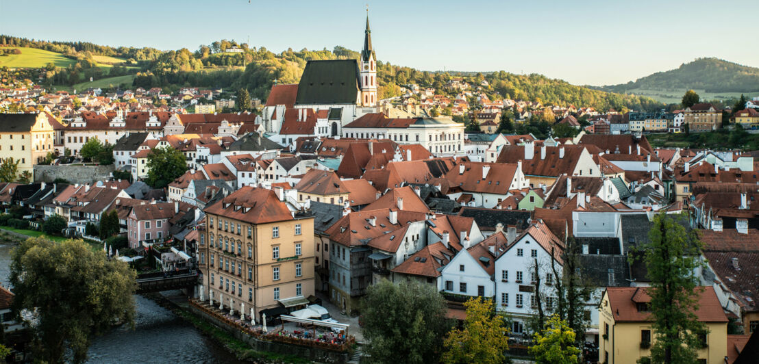 Mittelalterliche Kleinstadt an einem Fluss, im Hintergrund grüne Hügellandschaft.