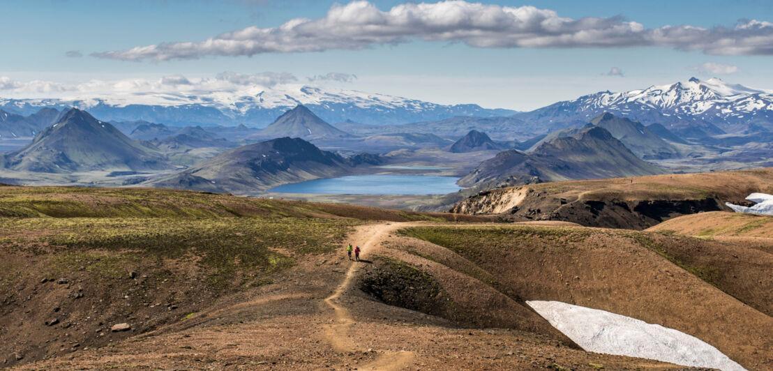 Landschaftspanorama in Island mit Trekkingpfad, auf dem sich zwei unkenntliche Personen befinden.