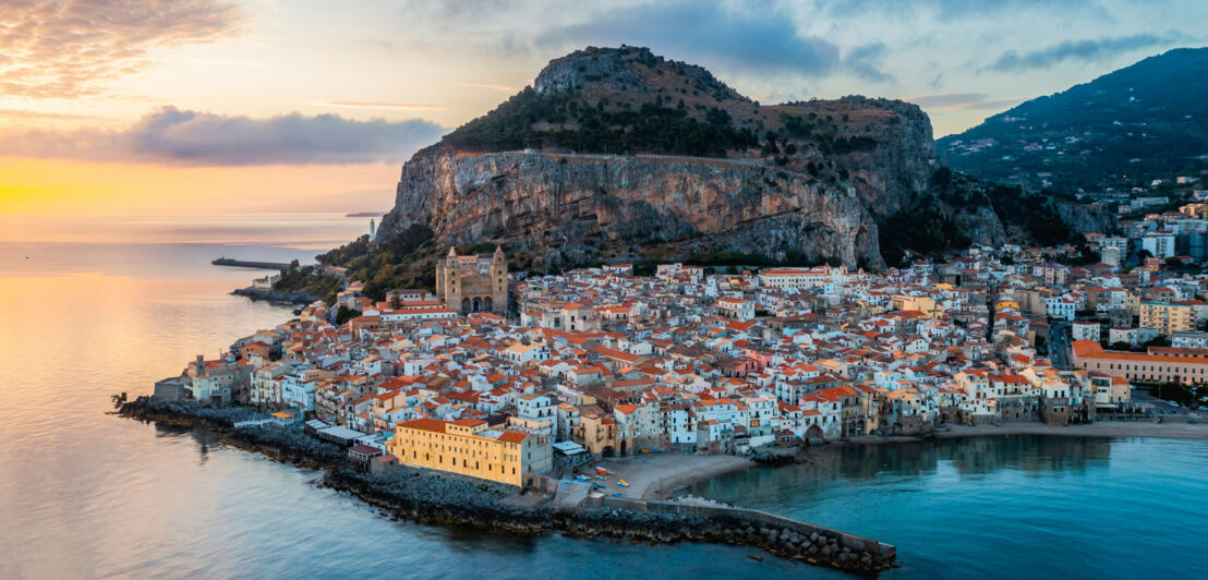 Mediterrane Stadt am Meer am Fuße eines Felsens mit Abendlicht. Mediterrane Stadt am Meer am Fuße eines Felsens mit Abendlicht.