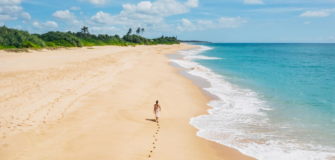 Rückansicht einer Frau, die einen breiten Sandstrand entlangläuft. Rückansicht einer Frau, die einen breiten Sandstrand entlangläuft.