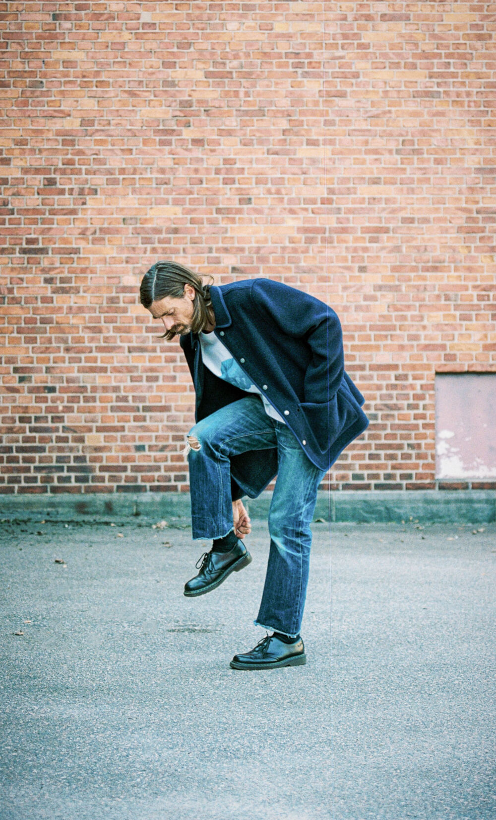 Ein Mann mit Jeanshose steht vor einer Backsteinwand