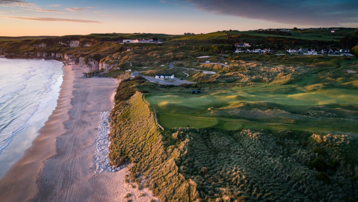 Blick auf einen Golfplatz und einen Küstenstreifen mit Sandstrand aus der Luft