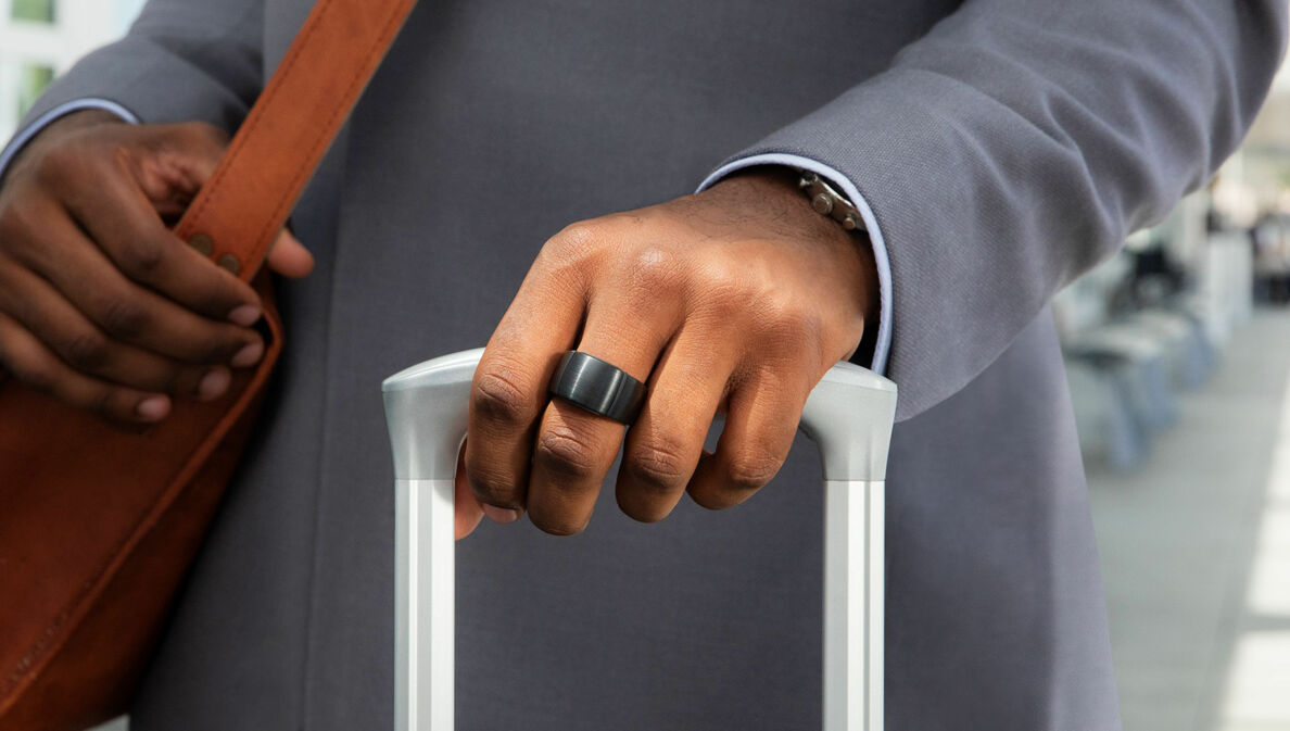 Ein Smart Ring am Mittelfinger einer Hand, die einen Trolley hält