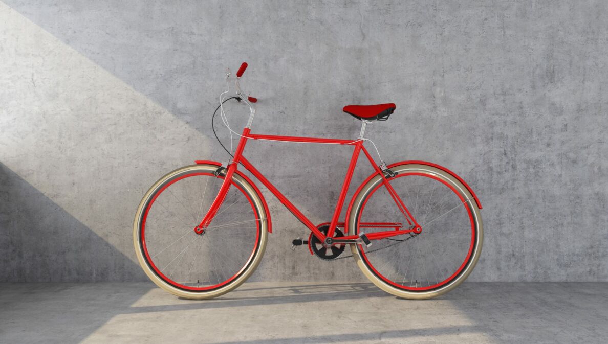 Ein orangefarbenes Designerfahrrad mit Ledersattel vor einer Betonwand