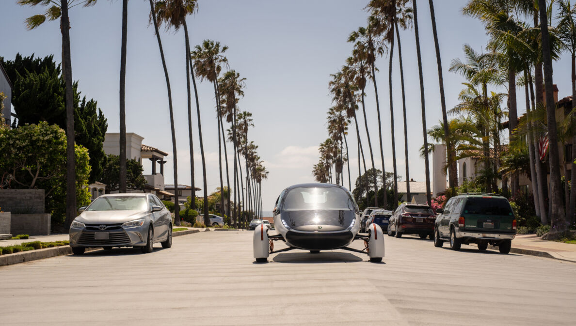 Ein futuristisches Fahrzeug fährt in der Sonne auf palmengesäumter Straße