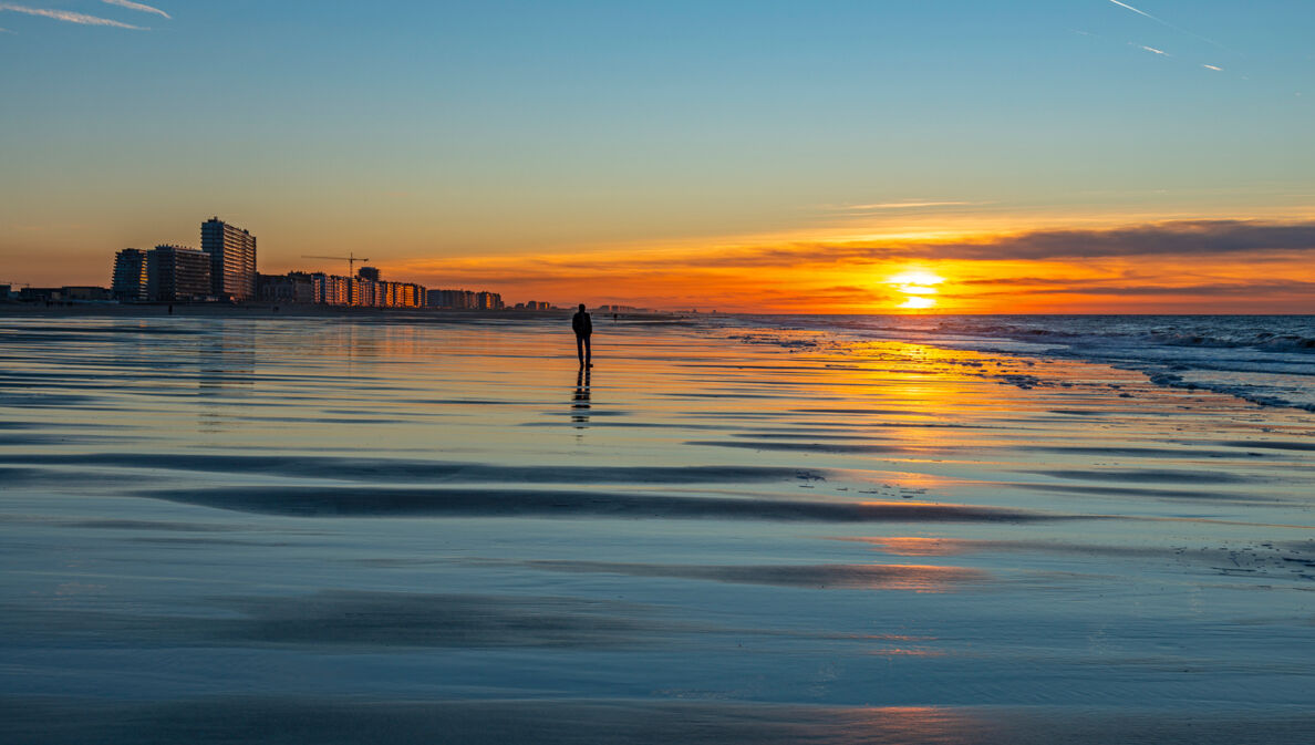 Eine Person am Strand bei Sonnenuntergang vor einer Stadt im Hintergrund