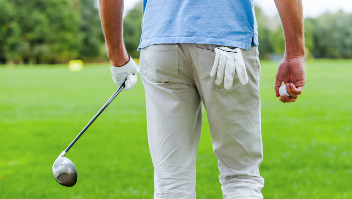 Rückansicht eines männlichen Golfspielers, der mit Golfball und Driver in der Hand weggeht