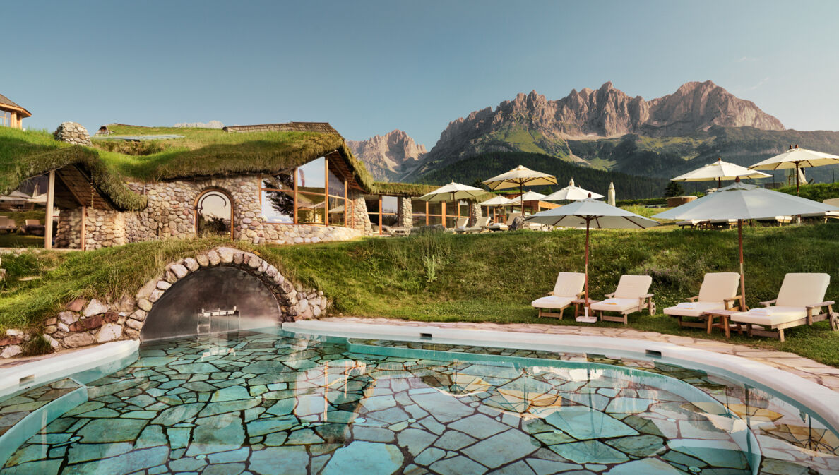 Hotelanlage mit begrüntem Dach und Liegen am Außenpool vor Bergpanorama