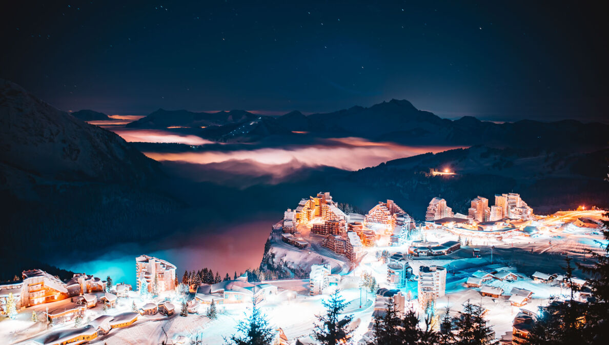 Eine erleuchtete Stadt bei Nacht, im Hintergrund dunkle Berge.