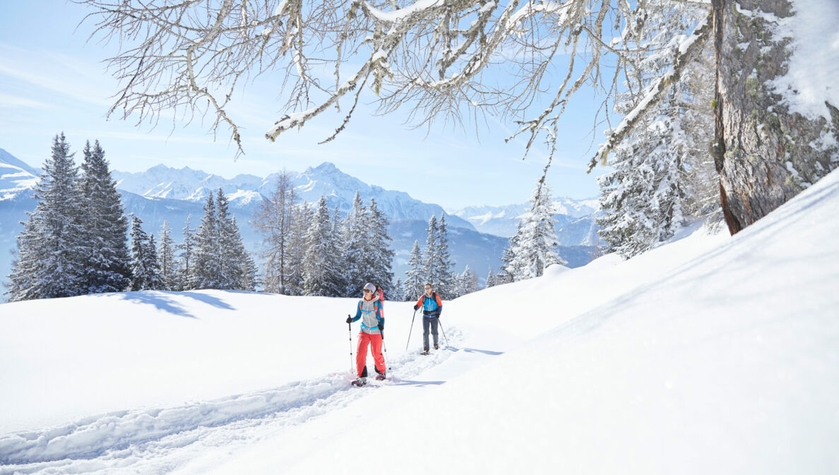 Zwei Wandernde mit Stöcken in einer verschneiten Berglandschaft