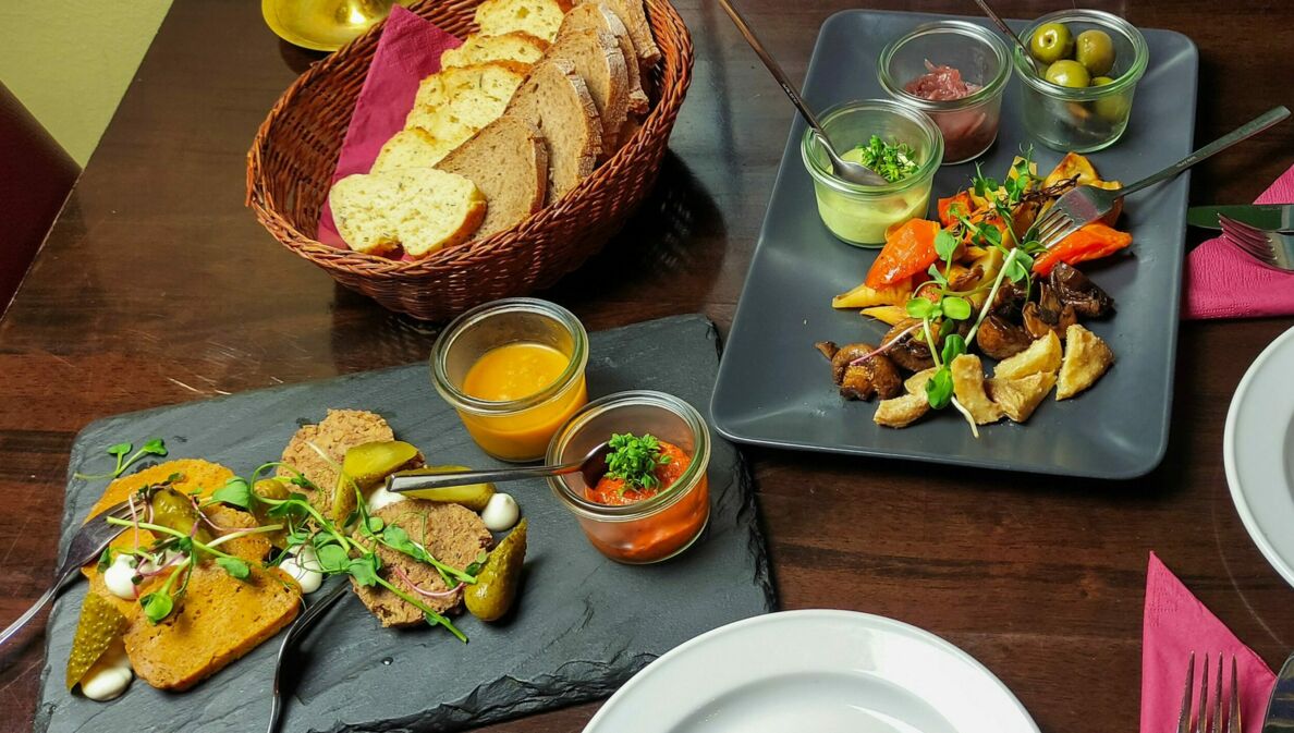 Vegane Tapas mit Dips und Brotkorb, angerichtet auf Servierplatten auf einem gedeckten Tisch