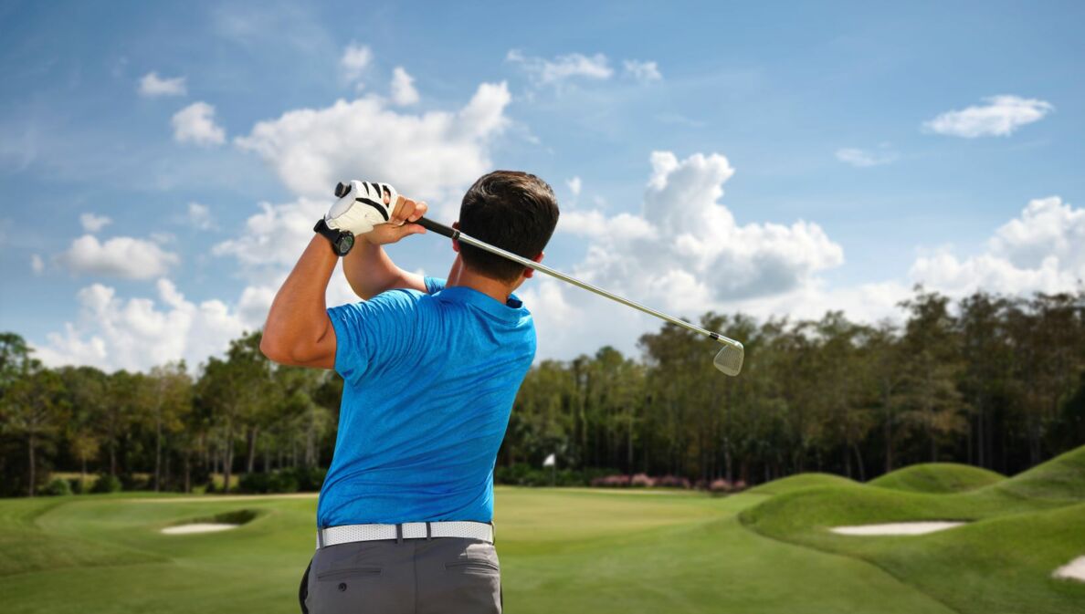 Ein Mann von hinten beim Abschlag auf einem Golfplatz