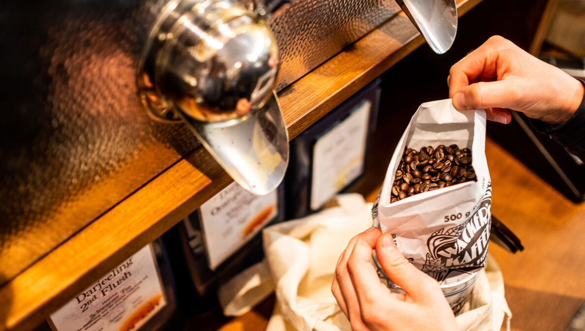 Nahaufnahme von zwei Händen, die in einem Geschäft einen Beutel mit Kaffeebohnen halten