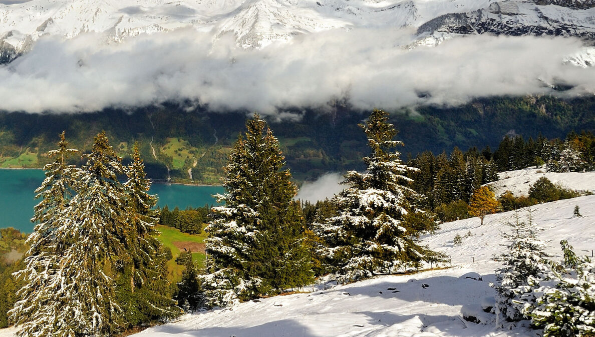 Schneebedeckte Berge, ein Bergsee und tiefhängende Wolken