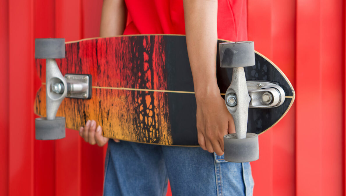 Rückansicht einer Frau, die ein Longboard hinter dem Rücken hält