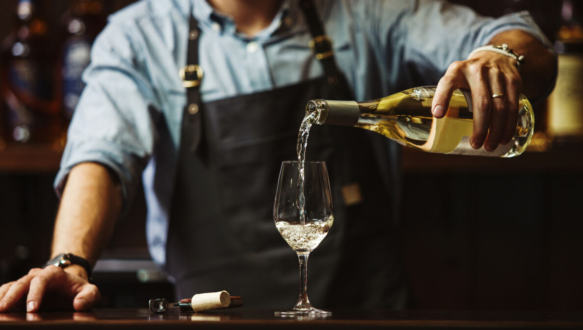 Ein Mann mit Schürze gießt Weißwein in ein Glas