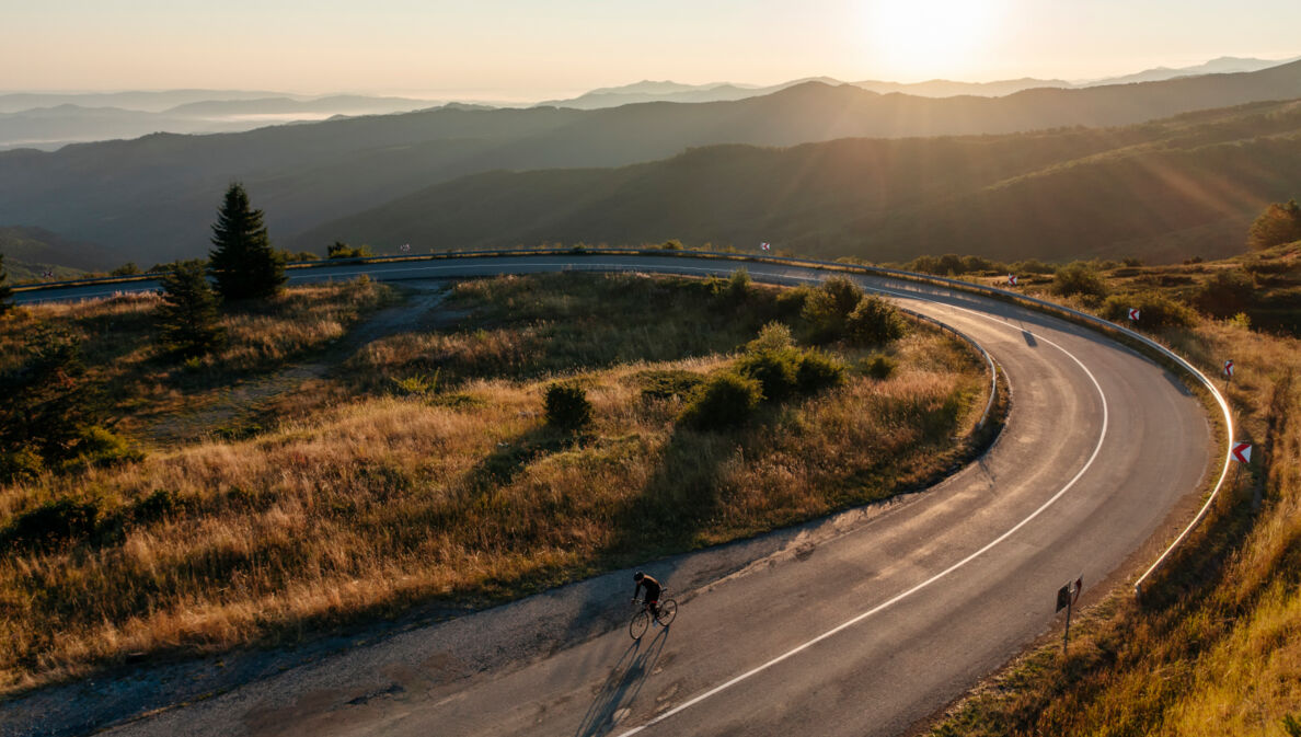 Ein Radfahrer auf einer einsamen Straße im Sonnenuntergang.