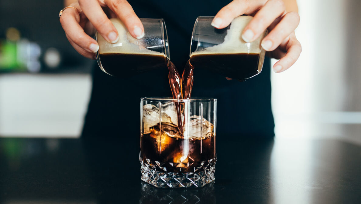 Eine Frau gießt kalten Kaffee in ein Glas mit Eiswürfeln