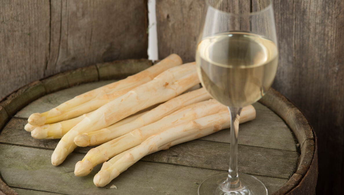 Ein Glas Wein und mehrere Stangen Spargel auf einem Fass Wein