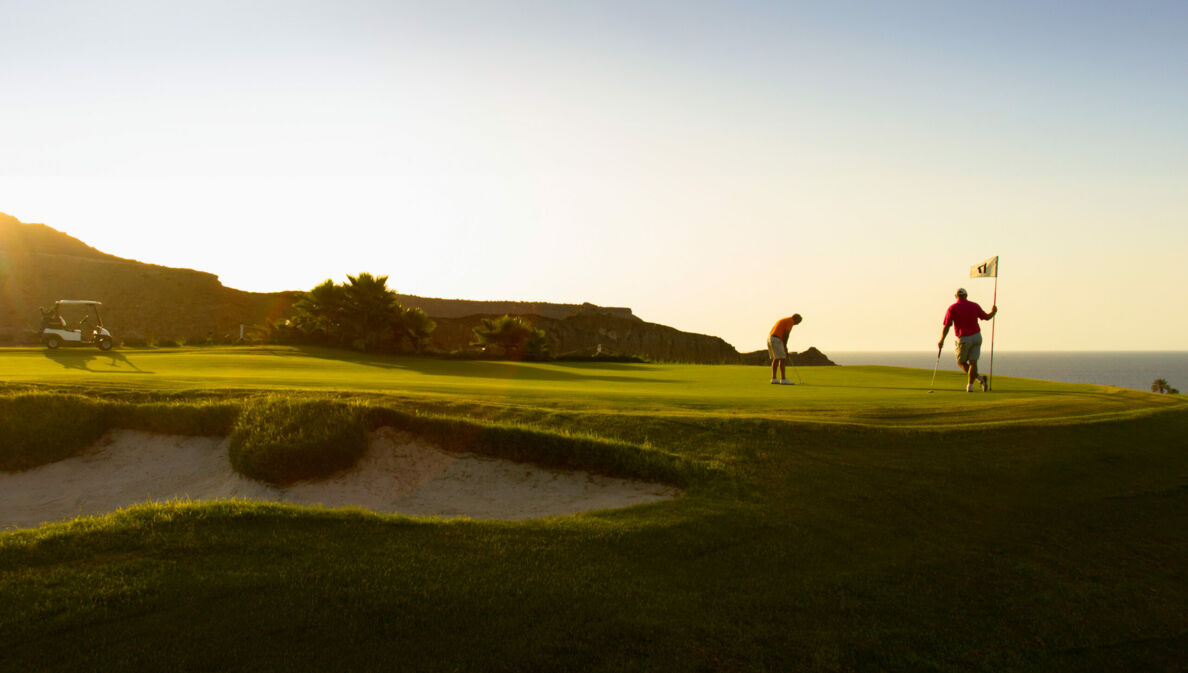 Zwei Golfspieler beim Abschlag auf einer Golfanlage im Sonnenuntergang