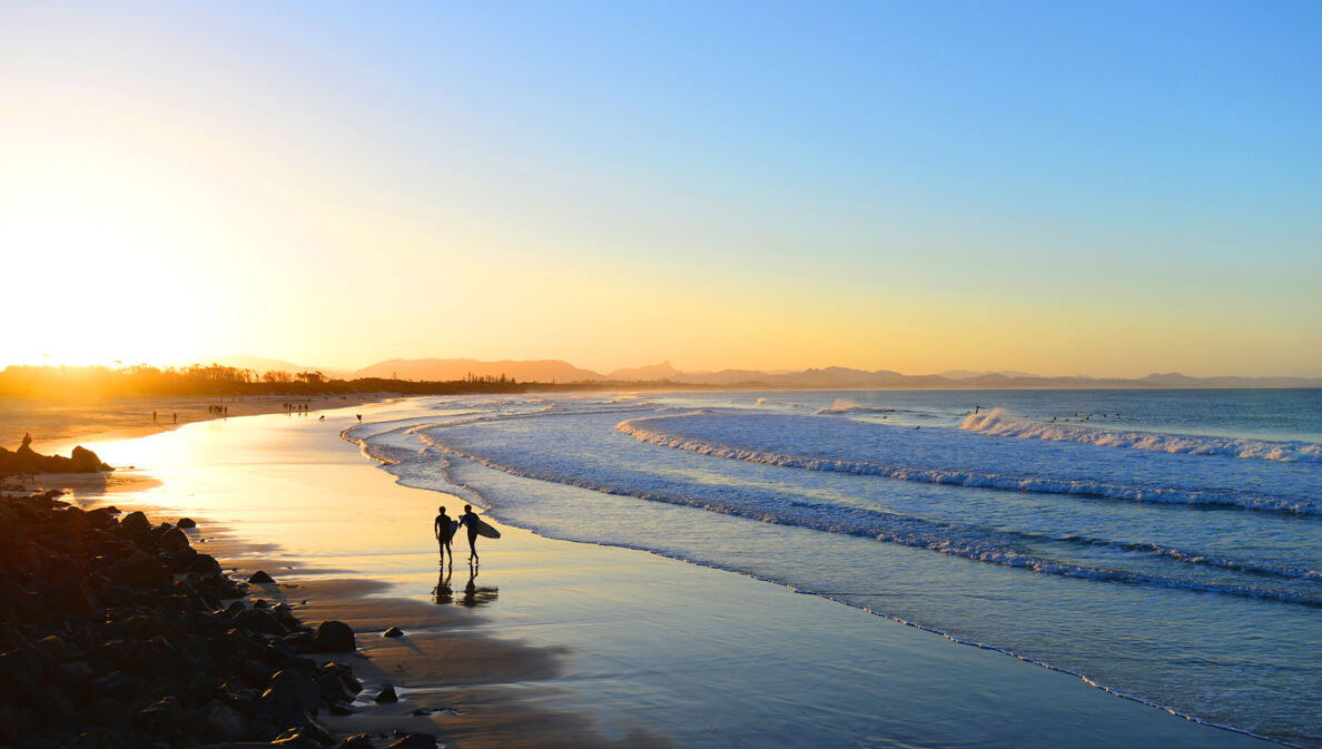 Ein Sandstrand im Ausland mit Surfern bei Sonnenuntergang