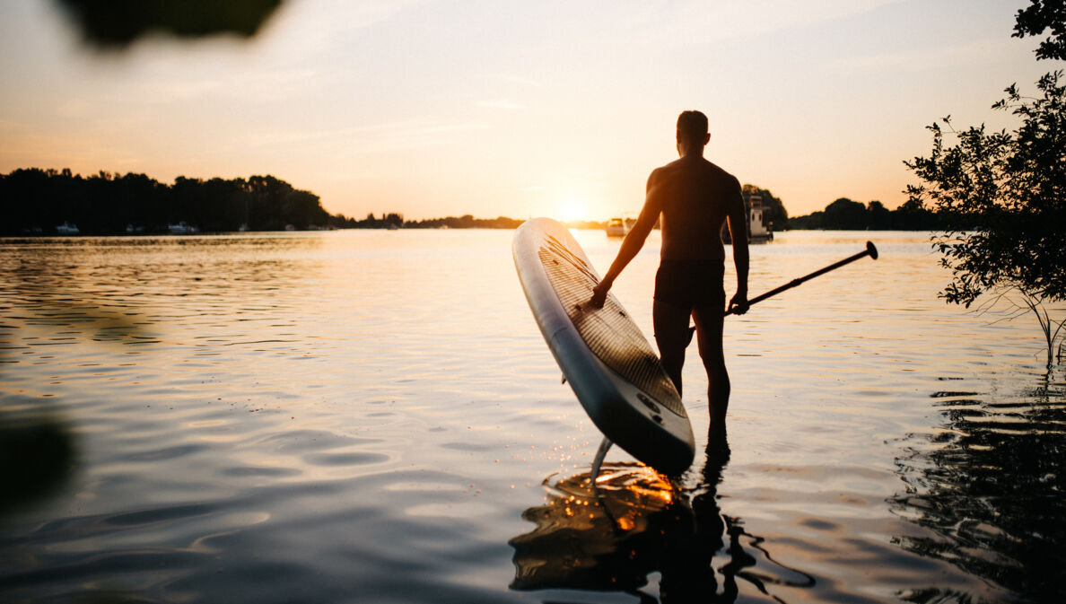 Mann trägt ein SUP Board ins Wasser