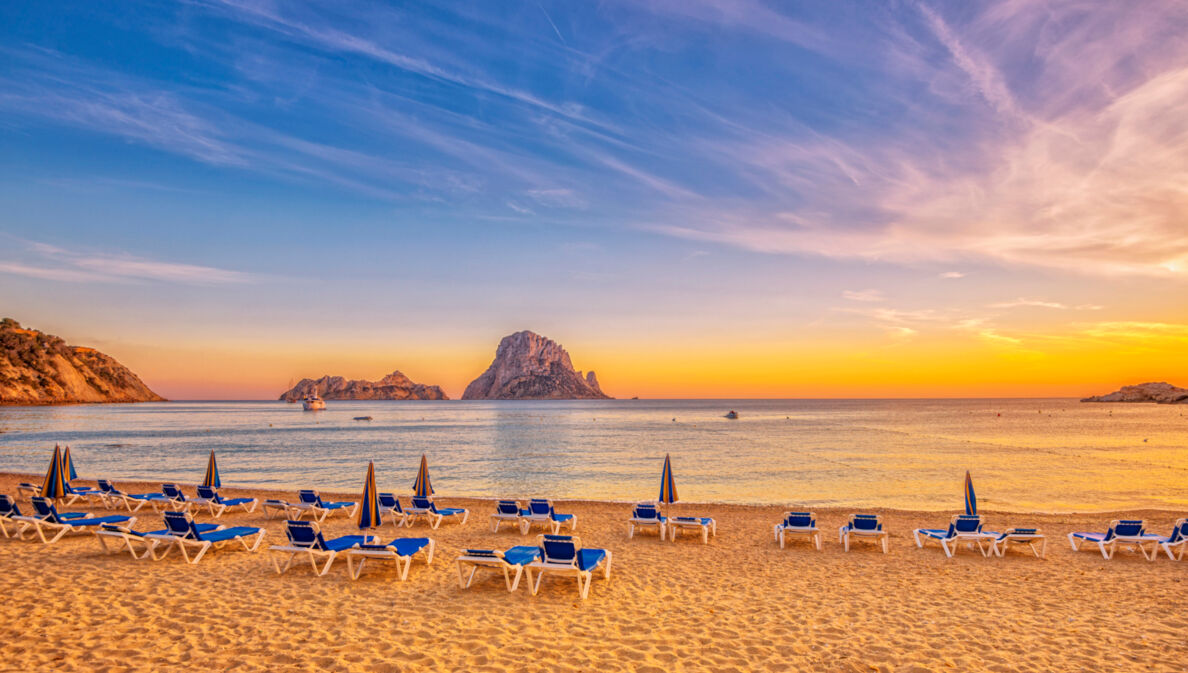 Ein Sandstrand mit Liegen bei Sonnenuntergang