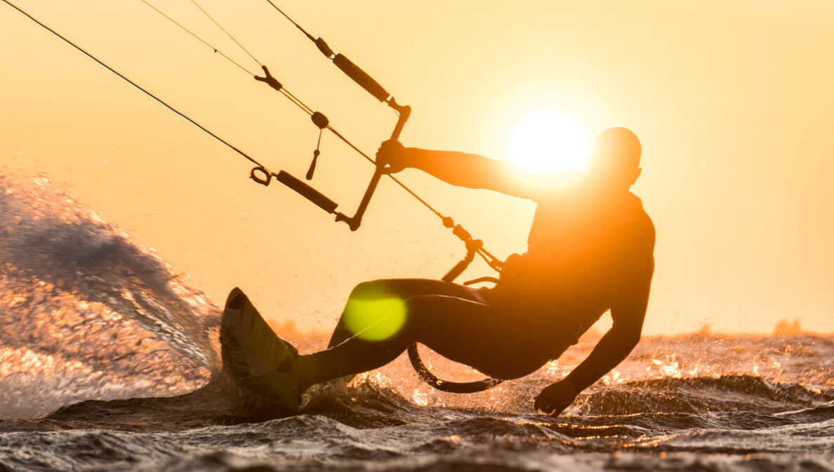 Silhouette des Kitesurfers, der bei schönem Sonnenuntergang mit Sonne neben dem Fahrerkopf reitet