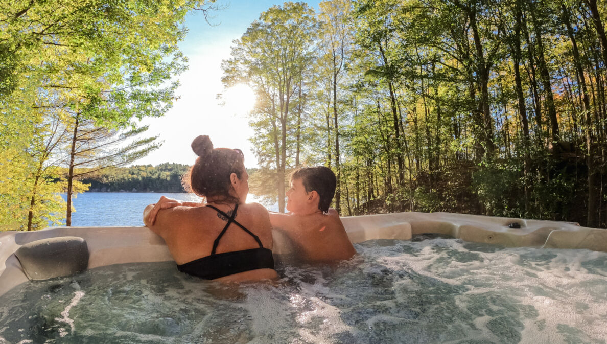 Mutter und Sohn entspannen im Outdoor-Whirlpool und blicken dabei auf einen See