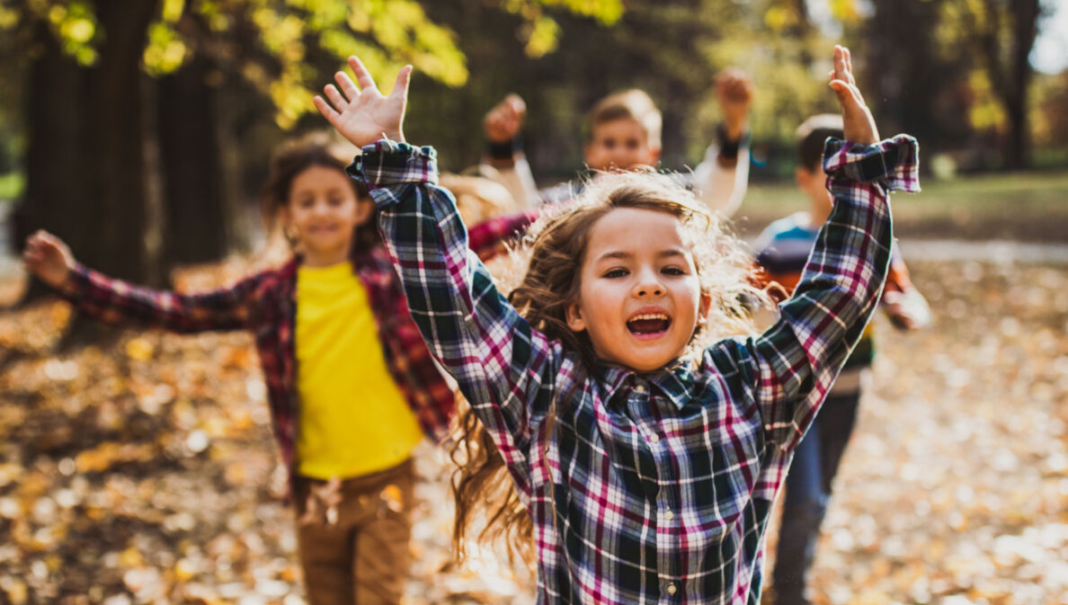 Vier fröhliche Kinder rennen im Freien durchs Laub