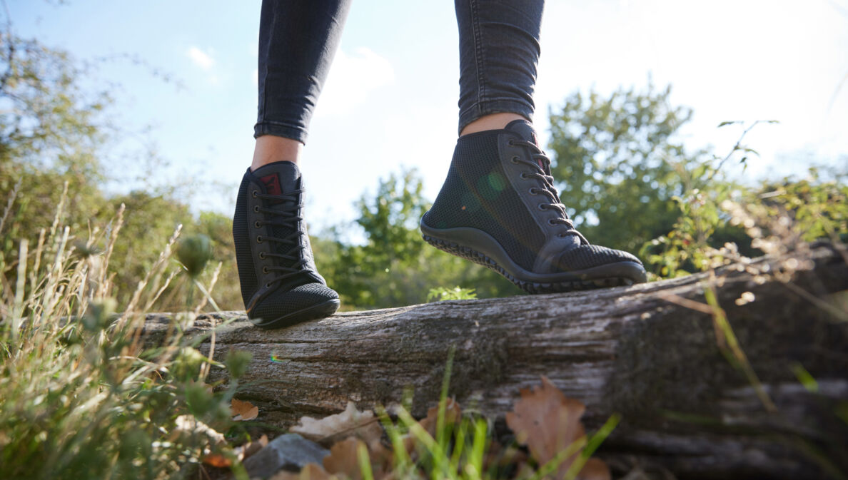 Eine balancierende Person in Barfußschuhen auf einem liegenden Baumstamm