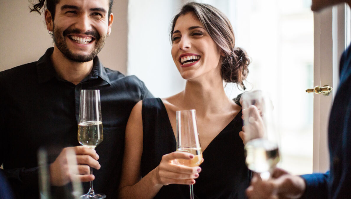 Ein fröhliches Paar in festlichen Outfits mit einem Glas Champagner in den Händen.