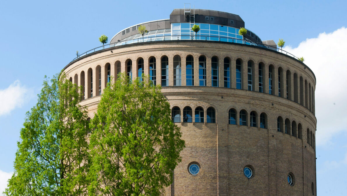 Ein runder, historischer Wasserturm mit moderner Terrasse