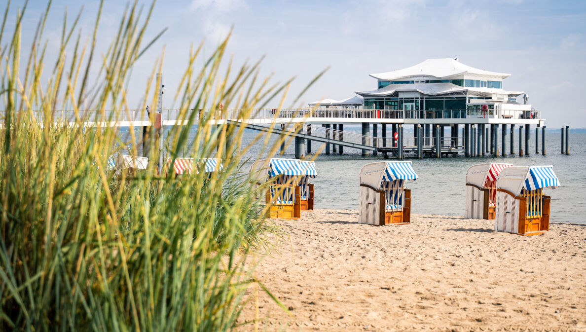 Blick vom Strand auf ein Haus, das im Wasser auf Stehlen steht.