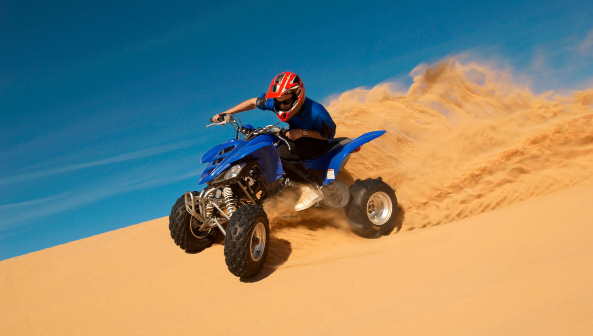 Ein Mann fährt auf einem Quad eine Sanddüne hinunter