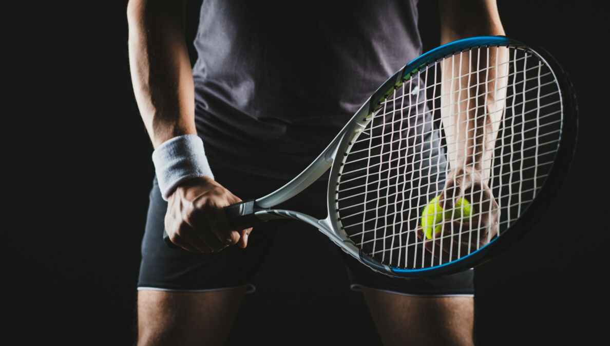 Eine Person hält einen Tennisschläger und Tennisball in der Hand.