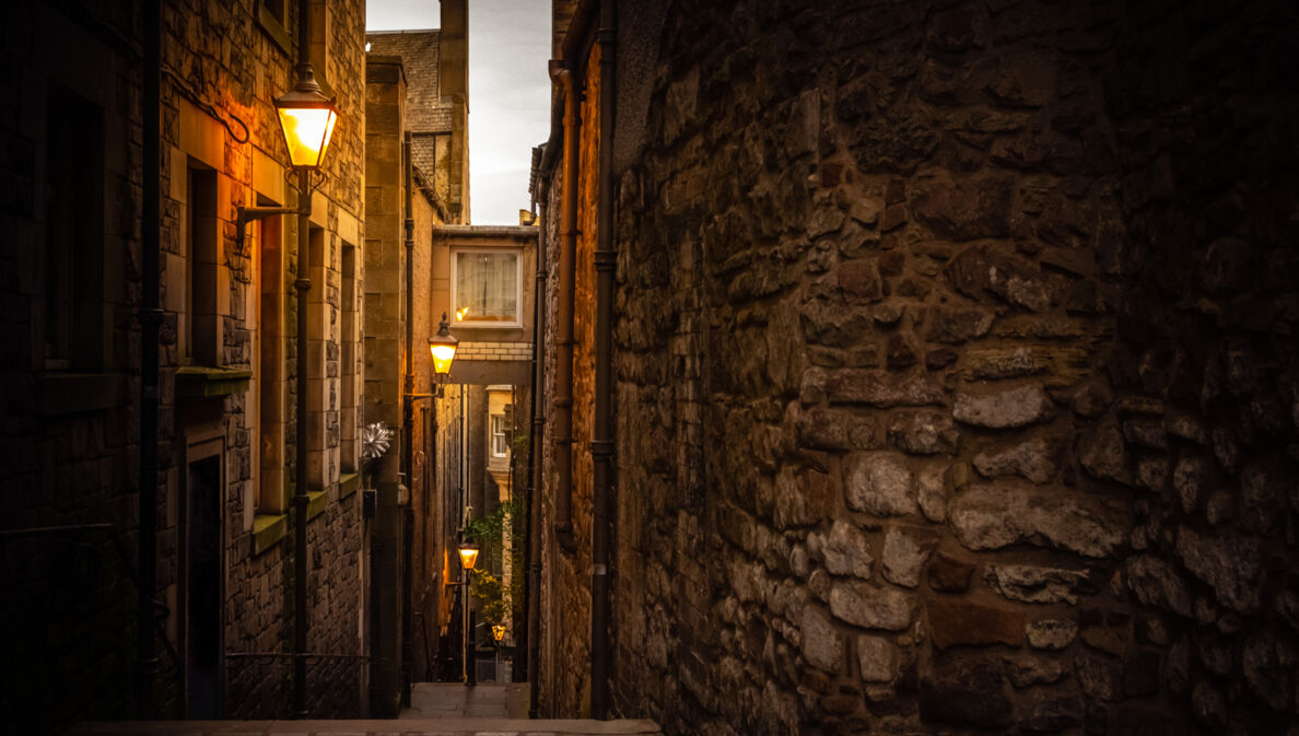 Dunkle Gasse in Edinburgh, die von Straßenlaternen schwach beleuchtet wird.