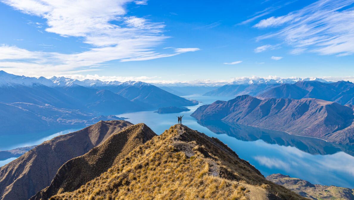 Ein Paar steht auf einem Gipfel vor Seenlandschaft und Bergpanorama der Neuseeländischen Alpen