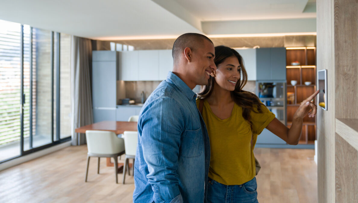 Zwei Personen stehen in einer modern eigenrichteten Wohnung und bedienen einen Touchscreen an der Wand