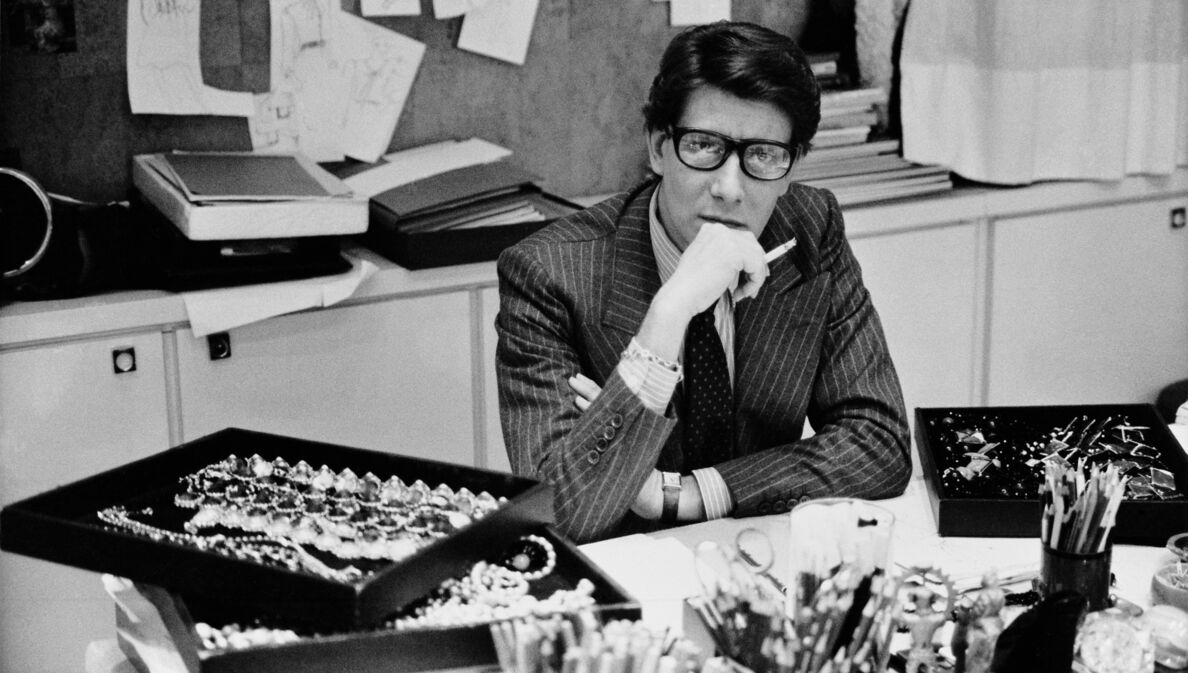 Schwarz-weiß-Aufnahme von Yves Saint Laurent an einem Schreibtisch in Paris 1986.