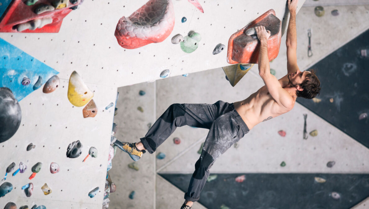 Ein durchtrainierter Mann an einer Kletterwand in einer Boulderhalle