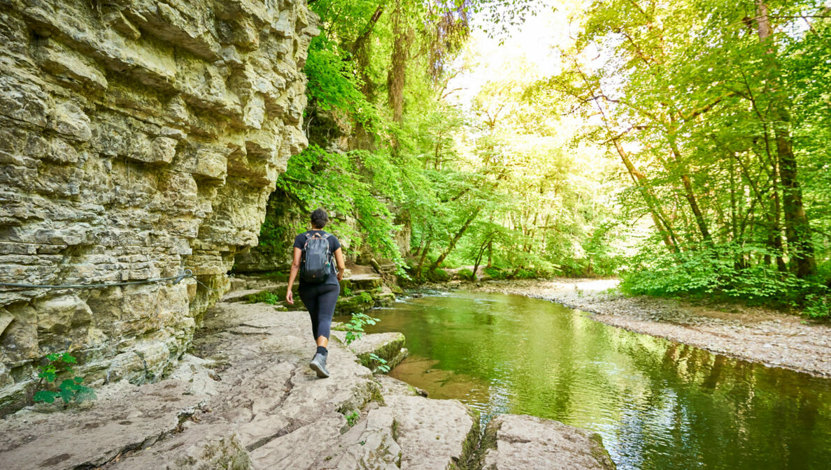 Eine Person mit Rucksack wandert an einem Fluss entlang