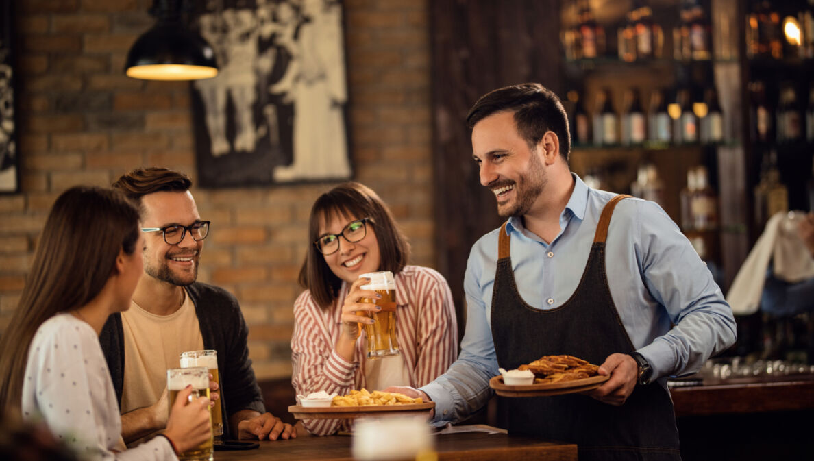 Lächelnder Kellner, der einer Gruppe von Gästen in einem Pub Essen bringt