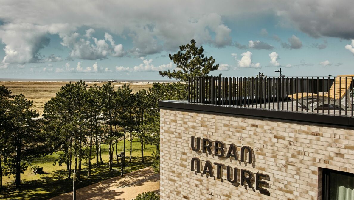 Blick auf die Dachterrasse des Urban Nature Hotels St. Peter Ording, im Hintergrund Bäume, Dünen, Meer und Wolken