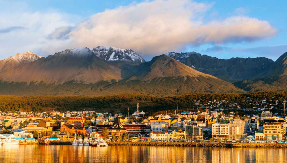 Stadtpanorama von Ushuaia am Wasser vor Bergkulisse im Sonnenuntergang