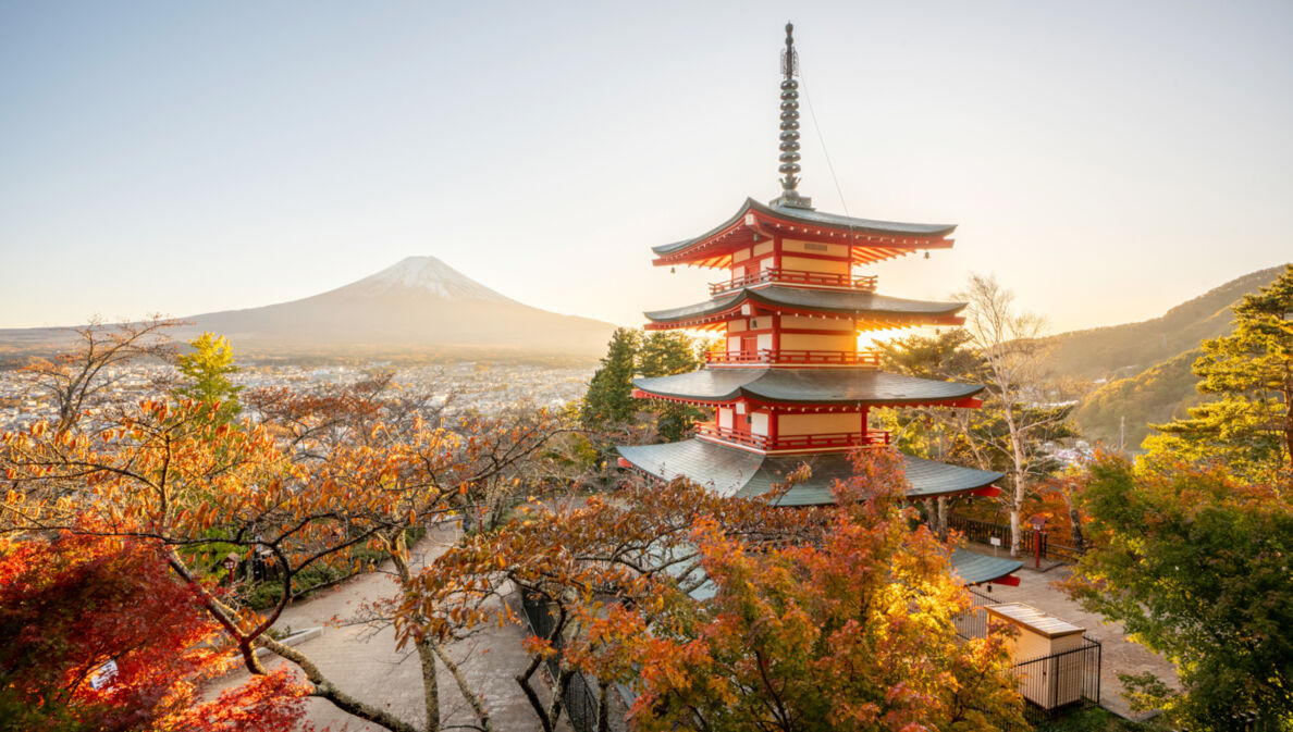 Ein mehrstöckiger, japanischer Tempel mit roten Ornamenten, im Hintergrund eine Stadt am Fuße des Mount Fuji