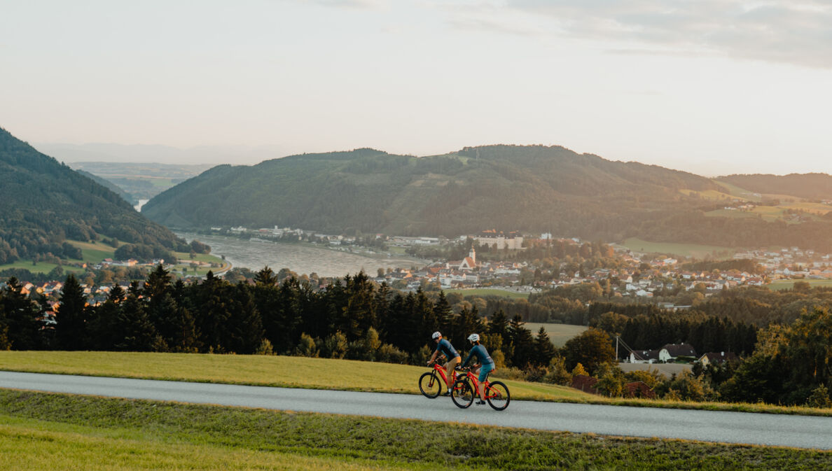 Zwei Radfahrer fahren auf dem Donauradweg mit Blick auf Berge